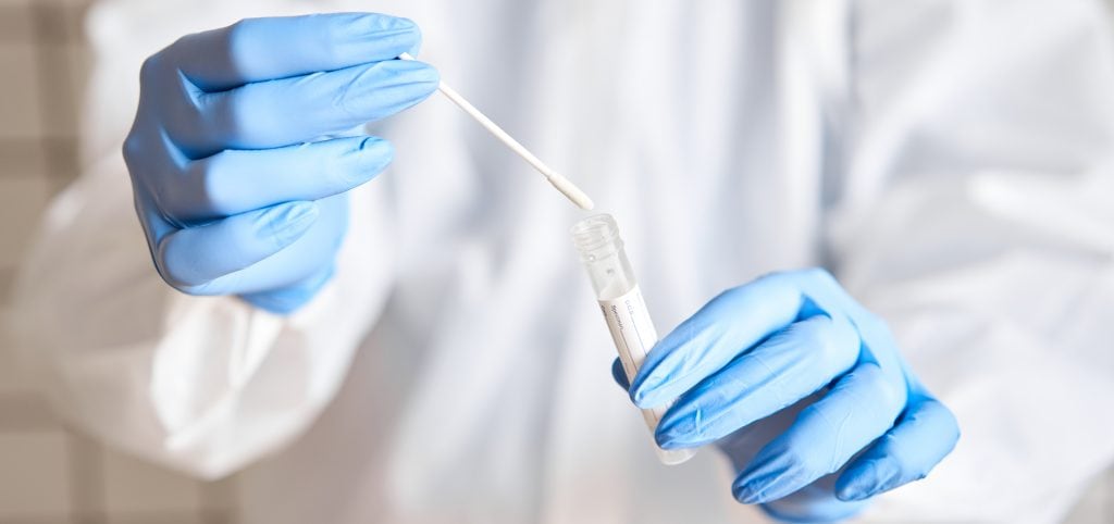 Doctor in PPE holding a swab and test tube.